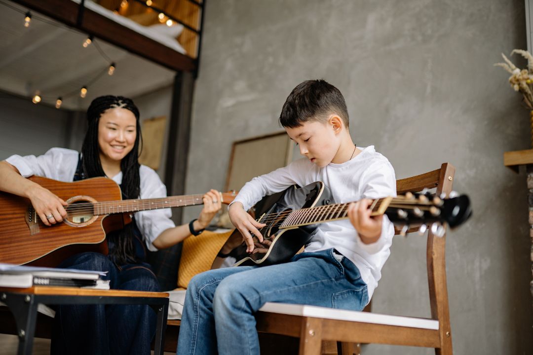 Mother and son playing guitar together, learning music at home for bonding and skill development | Learn The Art