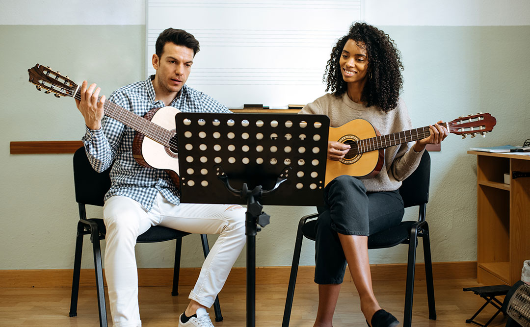 Man and woman taking a guitar lesson together, learning music in a classroom setting | Learn The Art