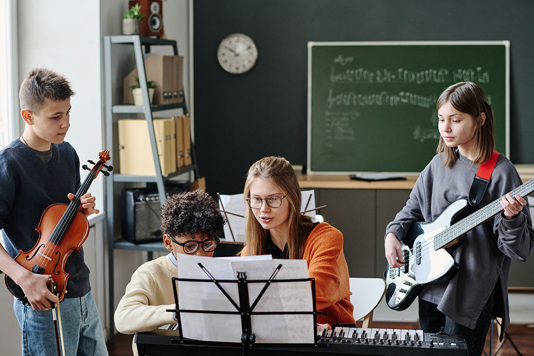 Group of kids learning music together in a classroom, playing violin, keyboard, and guitar | Learn The Art